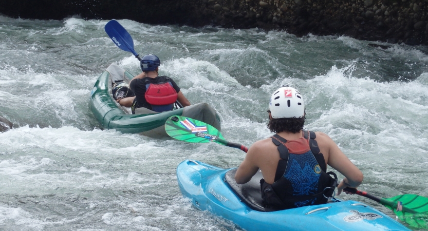 Two people wearing safety gear paddle two kayaks on whitewater. 